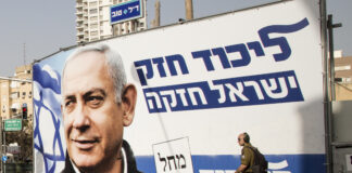 fotografia colori, esterno urbano diurno, grande manifesto elettorale di Benjamin Netanyahu con ritratto e scritte blu su sfondo bianco