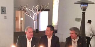 Fotografia colori, interno, 3 uomini seduti al tavolo con 3 centrotavola con candele accese, incontro formale presso ambasciata italiana in messico