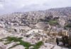 fotografia colori, panorama diurno città Amman, resti archeologici primo piano, sfondo edifici moderni su collina, colori chiari bianco grigio azzurro