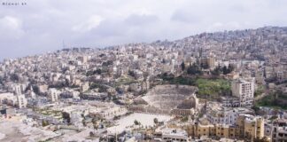 fotografia colori, panorama diurno città Amman, resti archeologici primo piano, sfondo edifici moderni su collina, colori chiari bianco grigio azzurro