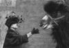 fotografia bianco nero, donna con cappotto e cappello con piume stende mano con guanto verso dromedario