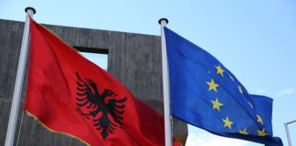 Fotografia colori, esterno, a sinistra bandiera albanese aquila nera due teste in campo rosso, a destra bandiera europea 12 stelle gialle in cerchio su campo blu