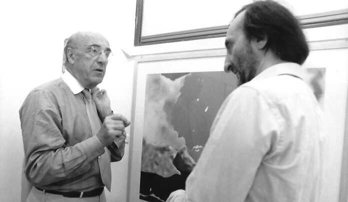 fotografia bianco nero biennale venezia 1997, interno, due uomini parlano davanti a quadro, a sinistra roger guillemin, a destra carmelo strano