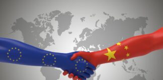 fotomontaggio, colori, due braccia si stringono la mano, braccio da sinistra colori bandiera europea, braccio da destra colori bandiera cinese, sfondo planisfero grigio