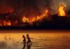 Due bambini sudamericani scappano in un bacino d'acqua. Sullo sfondo la foresta Amazzonica brucia.