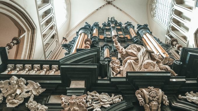 Abside di chiesa romana con organo e statue neoclassiche ripresa dal basso verso l'alto.