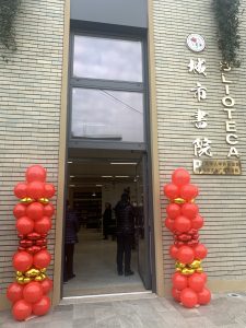L'ingresso della nuova biblioteca cinese di Prato, edificio in mattoni in stile cinese moderno, ai lati della porta due composizioni di palloncini rossi e oro a forma di torretta. Sulla parete alla destra della porta caratteri cinesi e italiani dorati
