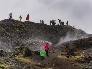 Turisti sparsi in uno scenario naturale selvaggio e avvolto dalla nebbia. Alcuni di loro fanno foto e scattano selfie.