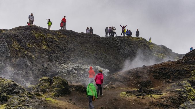 Turisti sparsi in uno scenario naturale selvaggio e avvolto dalla nebbia. Alcuni di loro fanno foto e scattano selfie.