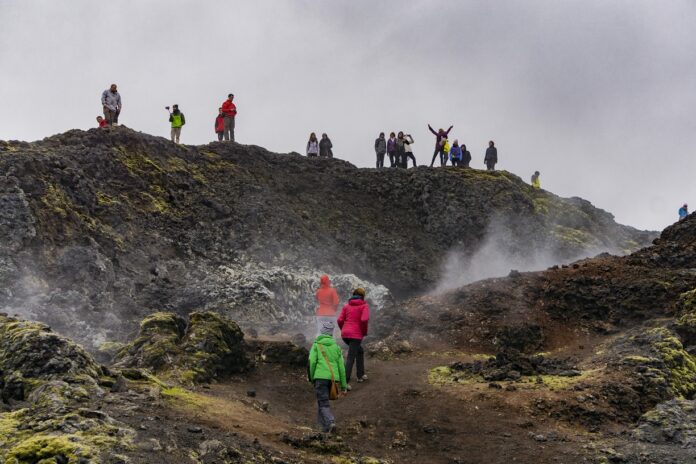 Turisti sparsi in uno scenario naturale selvaggio e avvolto dalla nebbia. Alcuni di loro fanno foto e scattano selfie.