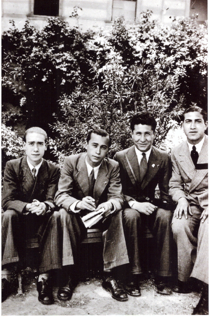 Black-and-white photography with 4 men in suits sitting on a bench, with shrubs on the background