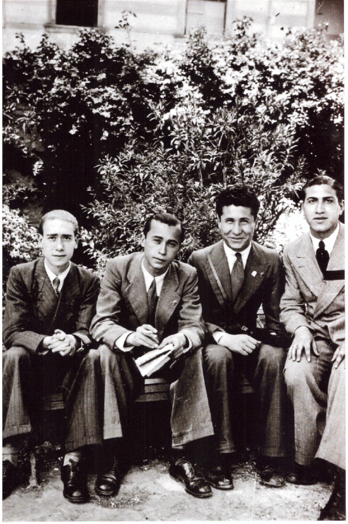 Leonardo Sciascia with his classmates Black-and-white photography with 4 men in suits sitting on a bench, with shrubs on the background