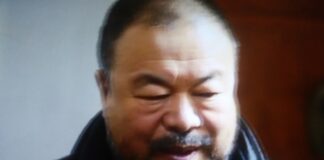 Foto sfocata di un uomo dai tratti orientali con lo sguardo basso e la bocca semi-aperta. L'uomo indossa una giacca blu