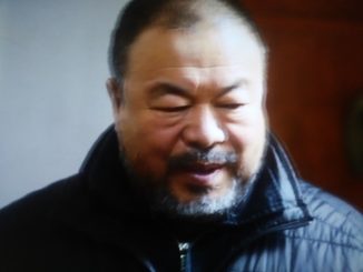 Foto sfocata di un uomo dai tratti orientali con lo sguardo basso e la bocca semi-aperta. L'uomo indossa una giacca blu