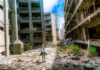 L'immagine mostra una ragazza al centro di una via di una città moderna in rovina, abbandonata dopo l'epidemia di Covid 19 Ai lati e sullo sfondo diversi palazzi diroccati occludono l'orizzonte tranne per un piccolo lembo di cielo in alto.