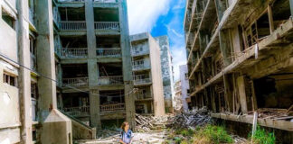 L'immagine mostra una ragazza al centro di una via di una città moderna in rovina, abbandonata dopo l'epidemia di Covid 19 Ai lati e sullo sfondo diversi palazzi diroccati occludono l'orizzonte tranne per un piccolo lembo di cielo in alto.
