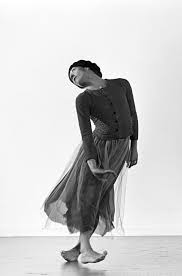 black and white photograph of the dancer Ana Laguna in the Mats Ek's Giselle, standing in an uneven pose wearing a tutu and a buttoned sweater.
