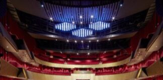 Interior of the Sheikh Jaber Al-Ahmed Cultural Center theater in Kuwait City, three-level hemicycle, with red armchairs and wooden structure.