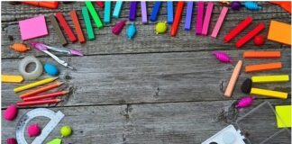 Matite colorate, pastelli a cera, tavolozza con colori all'acqua, un compasso, una calcolatrice, un temperino, un goniometro: strumenti di lavoro per uno scolaro, sparsi su un tavolo in legno.