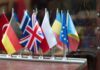 on a wood table there are twelve little flags in front of a reflecting surface. The visible flags are (from left to right) Turkey, germany, Greee, United Kingdom, Poland, Moldavia, European Union and Roumania
