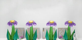 Quattro oggetti in plastica gonfiabile dalla forma di fiori con i petali viola sono disposti sopra quattro specchi