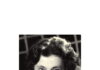 foto in bianco e nero e in primo piano di una donna con lo sguardo rivolto verso l'osservatore e il mento appoggiato sulla mano
