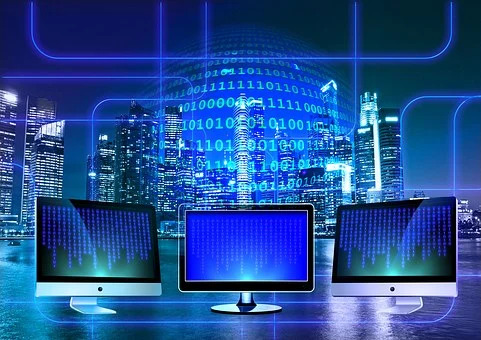 trasformazione digitale Tre monitor accesi da cui fuoriescono dei sottili fasci di luce blu. Al centro un gruppo di cifre luminose con alternanza di 0 e 1. Sullo sfondo grattacieli illuminati
