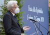 The picture shows Italian president Sergio Mattarella giving a speech in Codogno ( epicentre of the Covid-19 epidemy in Italy) on June 2nd. The president (in three-quarter profile) wears a dark blue jacket, a white shirt, a blue tie and the face mask. Behind the speaker and the microphone there are some palnts and a blue backdrop whit the white writing "Festa della Repubblica. Codogno 2 Giugno 2020" on it