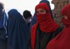 The photo shows several afghan women whose face is covered with a veil as in many muslim countries. The figures in the background wear traditional black and blue burqa. the two girl in the foreground, instead, wear a simpler red scarf that allows to see the eyes