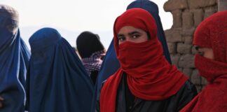 The photo shows several afghan women whose face is covered with a veil as in many muslim countries. The figures in the background wear traditional black and blue burqa. the two girl in the foreground, instead, wear a simpler red scarf that allows to see the eyes