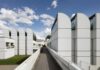 Under a blue, slightly cloudy sky, an architectural complex stands out formed by white, geometric blocks