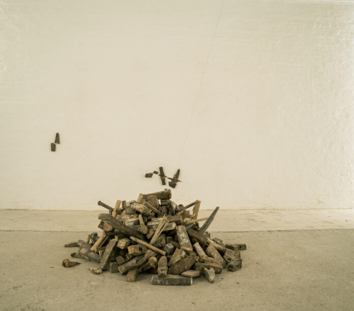 Utensili in legno, manici e teste di martelli raccolti in un mucchietto su un pavimento di mattonelle grigio chiaro, vicino a una parete bianca