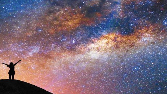Il principio antropologico di John Barrow cielo stellato invaso in buona parte da una luce gialla. In controluce sagoma di una persona in piedi con le braccia spalancate verso il cielo