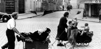 Photo from the 1940s: people on the street pushing prams containing an elder woman and children.