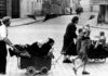 Foto degli anni 40 che ritrae gente in strada che cammina spingendo carrozzine contenenti anziani e bambini.