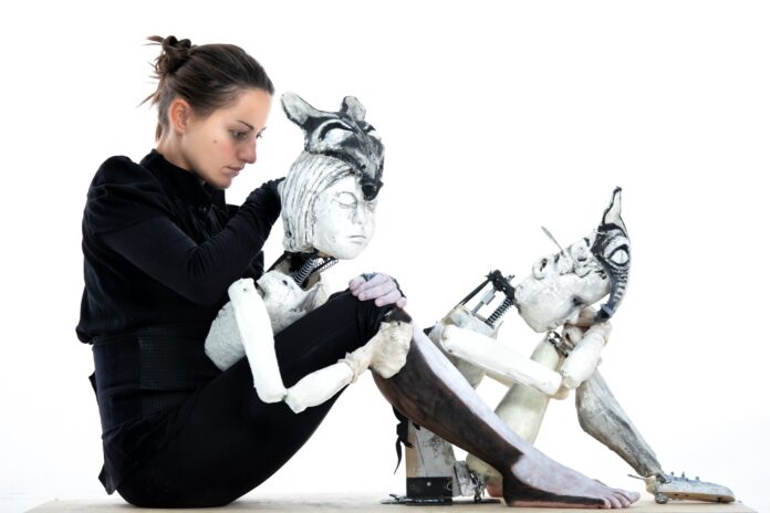 Fotografia della performer Marta Cuscunà seduta a terra con i suoi pupazzi.