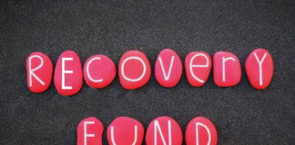 L'immagine mostra la scritta Recovery Fund in bianco. ciascuna lettera è all'interno di un ciottolo rosso ed i ciottoli sono disposti su una superficie scura simile ad asfalto