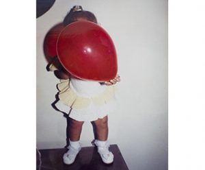 bimba con in mano un palloncino rosso davanti al volto