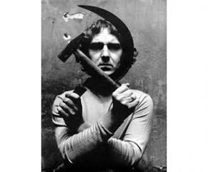 foto in bianco e nero di un uomo con le braccia incrociate che sostengono rispettivamente una falce e un martello
