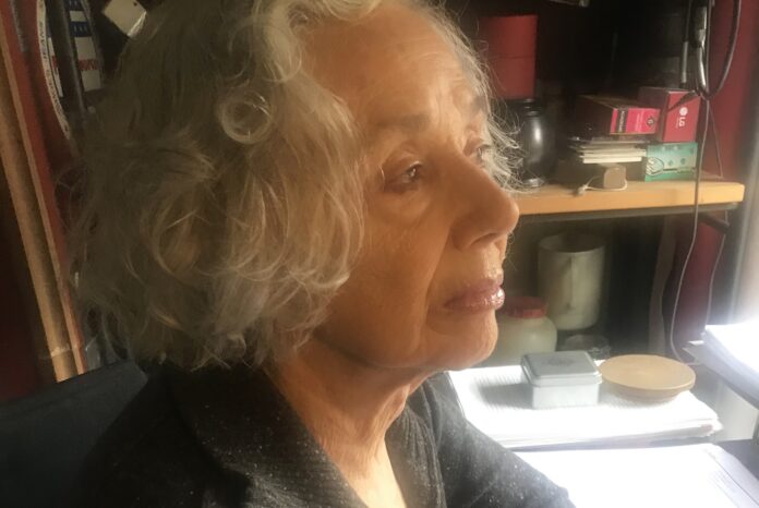 you can see a woman, the writer Alda Mercante, in front of her desk; her hair are white and she wears a blue jacket