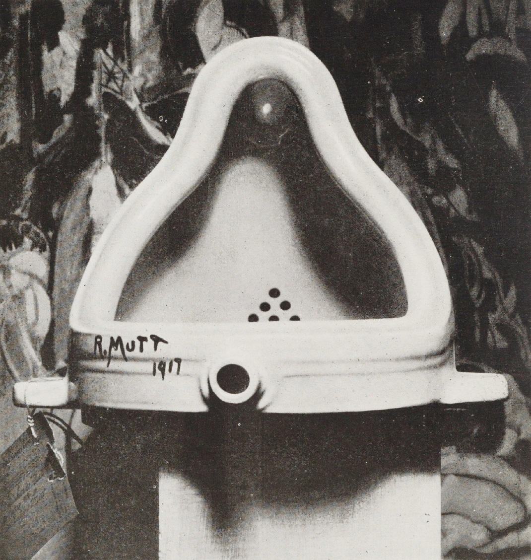 L'immagine è una foto in bianco e nero della celebre opera "Fontaine" di Marcel Duchamp, un orinatoio staccato e capovolto con una scritta nera nella parte inferiore "R.MUTT 1917"