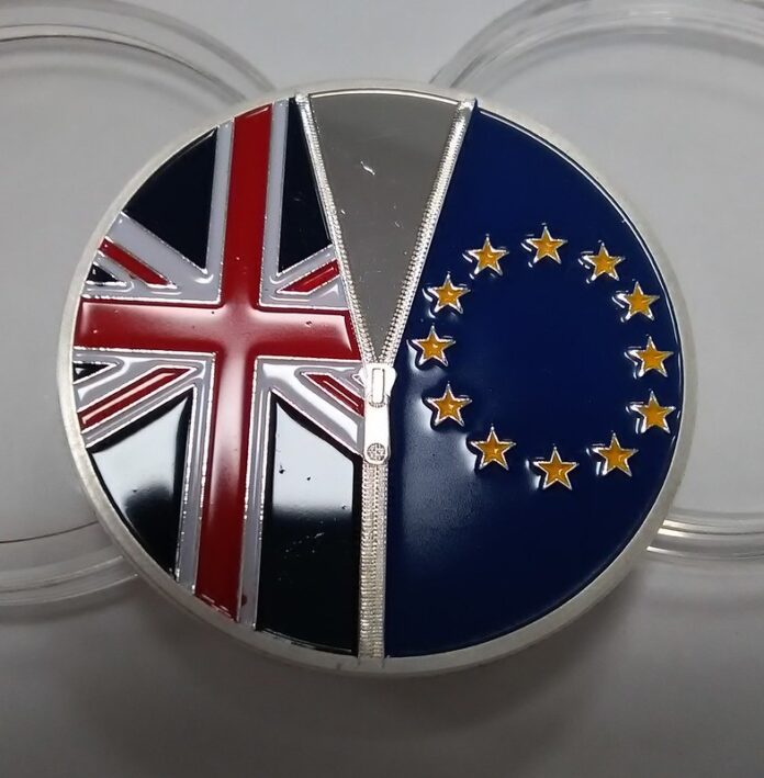 l'immagine mostra una medaglia metallica su cui sono incise le bandiere della union jack a sinistra e quela dell'Unione europea a destra, come se fossero du lati di una maglia, separata da una zip (anch'essa incisa)
