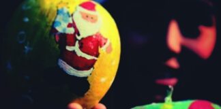 The picture shows a christmas tree yellow ball with a naive depiction of Santa Claus on it. Tha ball is reflected on a dark surface, whose limits are not clear