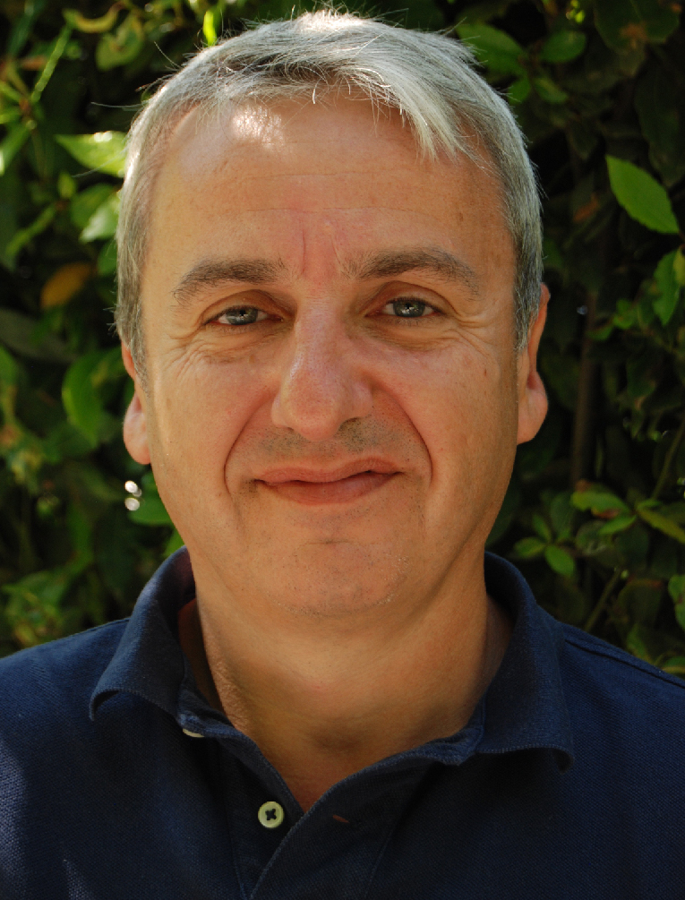 The photo is a portrait of french author Gilles Rozier. the man has white hairs, green eyes and a blue shirt. On the background ther's a green hedge