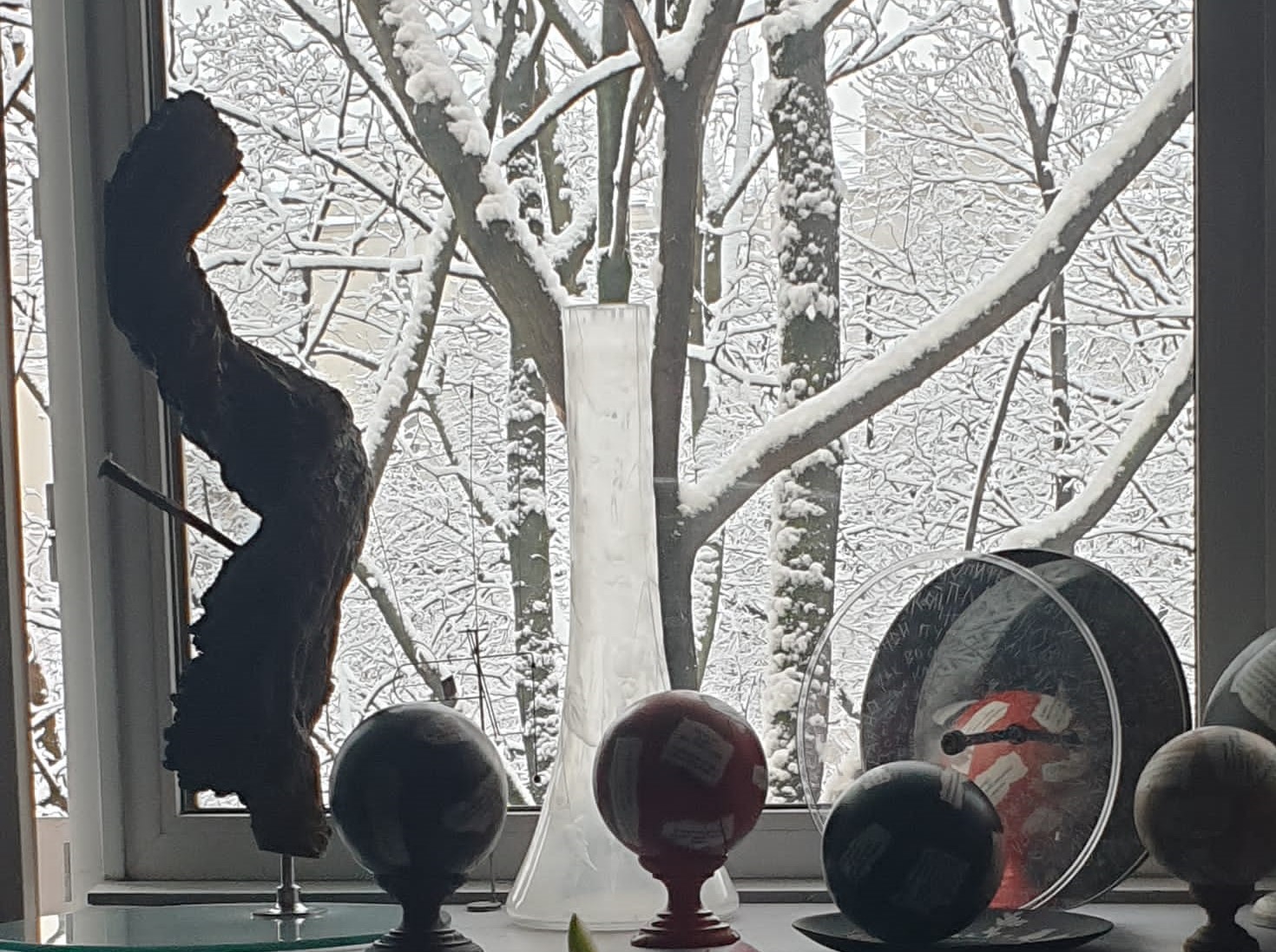 Evelina Schatz, Inverno, 2020 home page nella foto a colori si vedono alcune palle colorate con una base di legno, un vaso bianco trasparente, tutti poggiati sul davanzale di una finestra che si affaccia su uno spazio esterno innevato