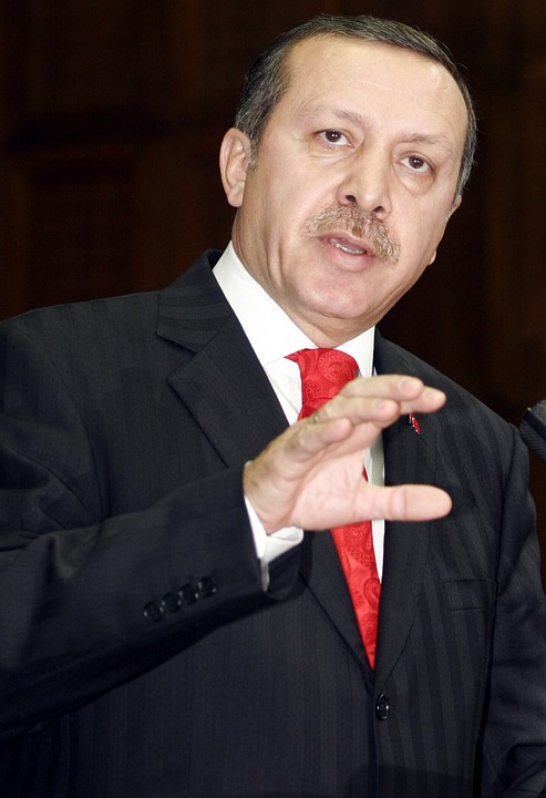 nella foto a colori si vede il Presidente della Turchia Recep Tayyip Erdoğan che indossa una giacca nera e una cravatta rossa; sta parlando a qualcuno.