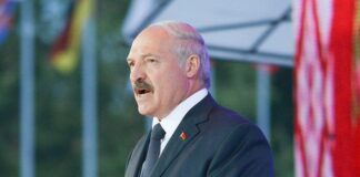 nella foto a colori si vede il dittatore bielorusso Alexander Lukashenko che tiene un discorso di fronte ad una pedana e un microfono; indossa completo scuro e cravatta scura, o blu o nero.
