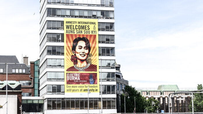 nella foto a colori si vede un edificio sul quale è stato affisso un poster di Amnesty International con l'immagine della leader Aung San Suu Kyi