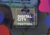 nella foto a colori si vede il logo del Digital City Festival, con questa scritta all'interno di un quadrato, e una persona che, girata di spalle, tra guardando un gioco elettronico