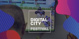nella foto a colori si vede il logo del Digital City Festival, con questa scritta all'interno di un quadrato, e una persona che, girata di spalle, tra guardando un gioco elettronico